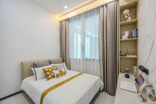 Cozy bedroom with a bed, decorative pillows, shelves, and a laptop on a desk