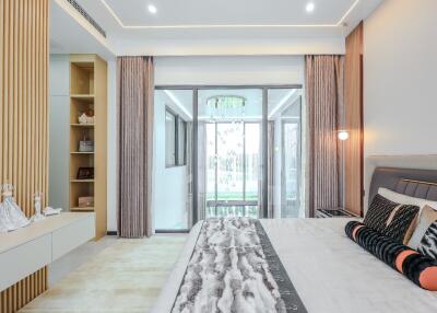 Modern bedroom with large bed, decorative cushions, built-in shelves, and sliding glass doors leading to a balcony