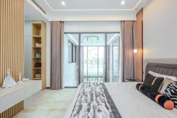 Modern bedroom with large bed, decorative cushions, built-in shelves, and sliding glass doors leading to a balcony