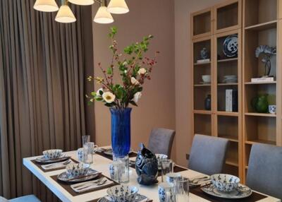 Elegant dining room with a modern chandelier, set dining table, and wooden shelves.