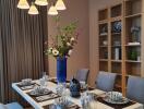 Elegant dining room with a modern chandelier, set dining table, and wooden shelves.