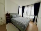 A tidy bedroom with a bed, nightstand and large windows with curtains