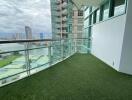 Spacious balcony with artificial grass flooring and glass railing, offering city and water views