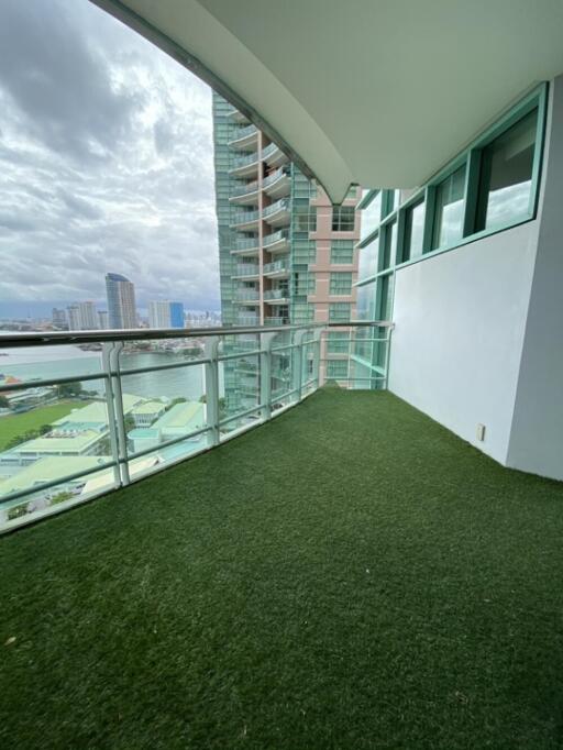 Spacious balcony with artificial grass flooring and glass railing, offering city and water views