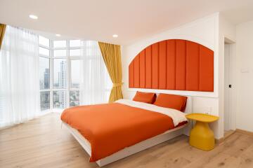 Bright modern bedroom with large windows, red and white bedding, yellow nightstand, and wooden flooring.