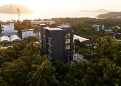 Aerial view of a modern building surrounded by lush greenery with a seaside sunset backdrop