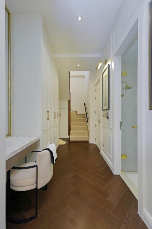 Elegant hallway with white walls, dark wooden flooring, and a staircase leading to the upper floor.