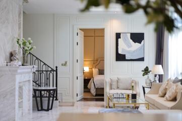 Elegant living room with marble fireplace, staircase, and view into a bedroom