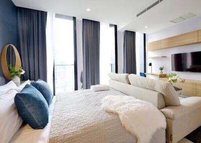 Modern bedroom with large windows, sofa, and television