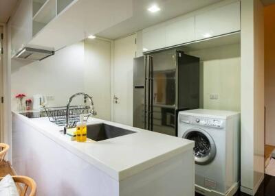 Modern kitchen with white countertops, washing machine, and refrigerator