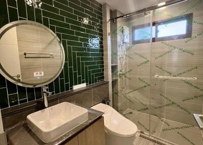 Modern bathroom with green tiled accent wall, round mirror, glass-enclosed shower, and contemporary fixtures.