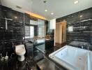 Modern bathroom with black marble walls, a large bathtub, glass shower, and toilet