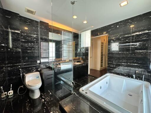 Modern bathroom with black marble walls, a large bathtub, glass shower, and toilet