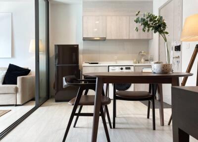 Modern kitchen and dining area with wooden dining table and chairs, integrated fridge, washer, sink, and cabinetry