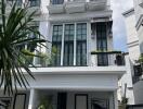 Front view of a multi-storey white building with balconies and potted plants