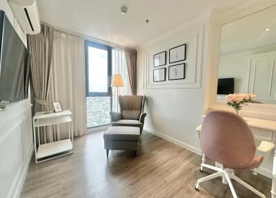 Cozy living room with a chair, ottoman, TV, and desk near a window.