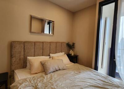 Bedroom with beige padded headboard, bedside tables, wall mirror, and access to balcony