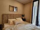 Bedroom with beige padded headboard, bedside tables, wall mirror, and access to balcony