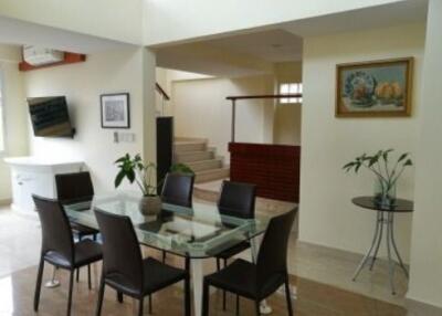 Modern dining area with a glass table and dark chairs, adjacent to a stairway