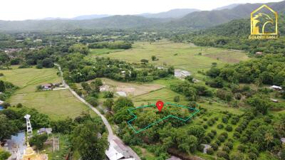 Aerial view of a vast rural land with greenery, hills in the background, and a property marked with a pin.