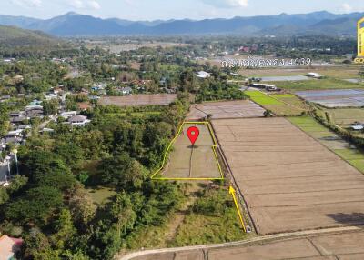 Aerial view of a plot of land surrounded by fields and mountains in the background