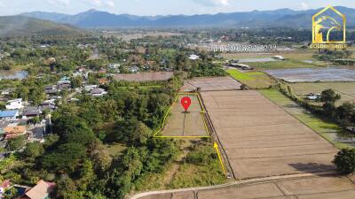 Aerial view of a plot of land surrounded by fields and mountains in the background