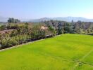 Aerial view of a large green field with surrounding trees and distant mountains