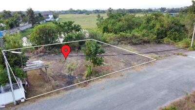 A vacant land plot with a marked location, surrounded by greenery and adjacent to a road