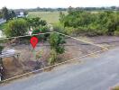 A vacant land plot with a marked location, surrounded by greenery and adjacent to a road