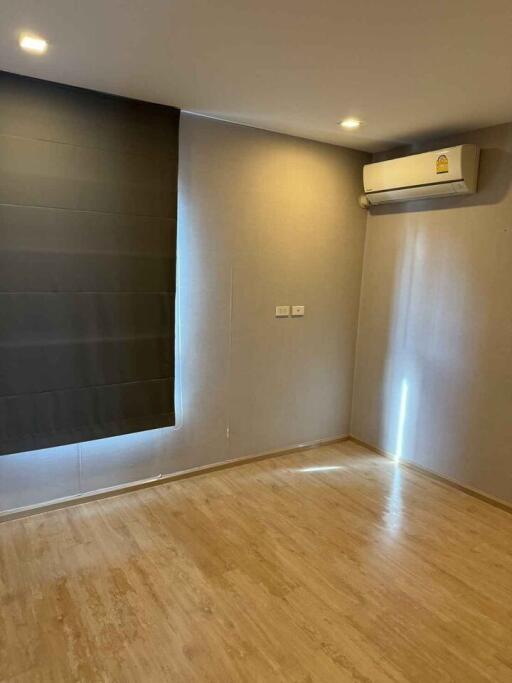 Empty bedroom with wooden floors, window with a dark curtain and a split air conditioning unit