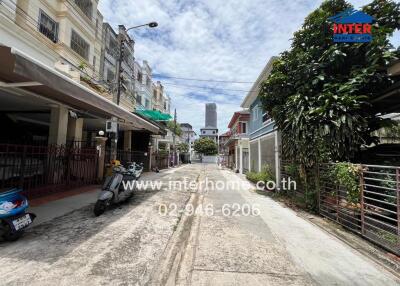 Street view of neighborhood with row houses, greenery, and a scooter