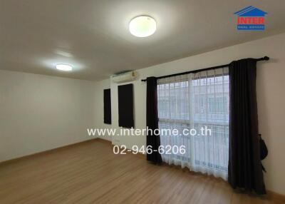 Spacious living room with wooden floor, large windows covered with black curtains and an air conditioning unit.