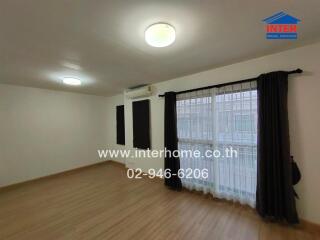 Spacious living room with wooden floor, large windows covered with black curtains and an air conditioning unit.