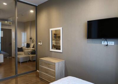 Bedroom with wall-mounted TV, wooden dresser, and mirror