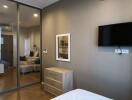 Bedroom with wall-mounted TV, wooden dresser, and mirror