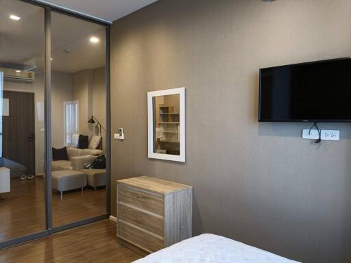 Bedroom with wall-mounted TV, wooden dresser, and mirror