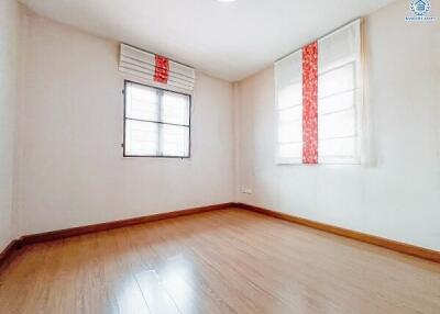 Empty bedroom with wooden floor and two windows with blinds and curtains