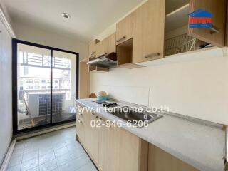 Modern kitchen with light wooden cabinets, countertop with sink and electric stove, and an adjacent balcony