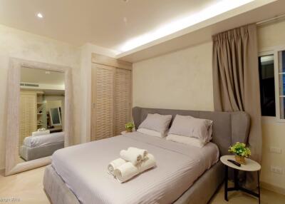 Modern bedroom with double bed, neatly made with pillows and towels, and warm lighting