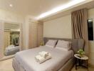 Modern bedroom with double bed, neatly made with pillows and towels, and warm lighting