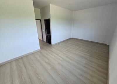 Spacious empty bedroom with light wood flooring and neutral walls