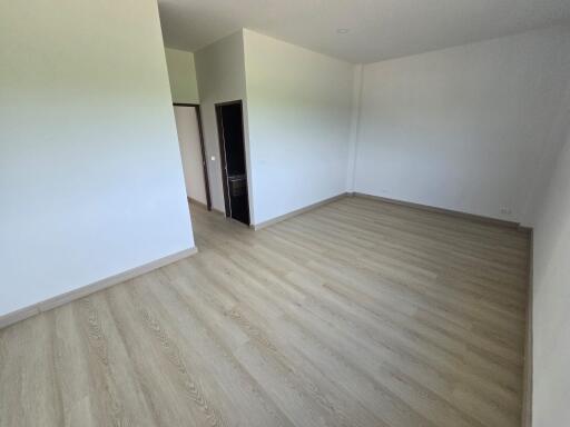 Spacious empty bedroom with light wood flooring and neutral walls