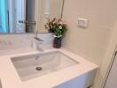 Modern bathroom sink area with mirror and flowers