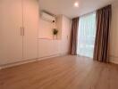 Spacious bedroom with wooden flooring, large window, built-in wardrobes, and air conditioning