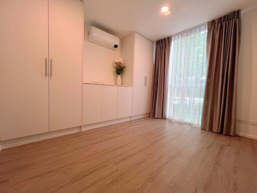 Spacious bedroom with wooden flooring, large window, built-in wardrobes, and air conditioning