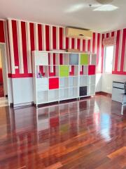 A brightly painted bedroom with striped walls, wooden flooring, and a colorful storage unit.