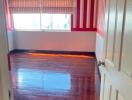 Empty bedroom with wooden floor and striped red and white wallpaper