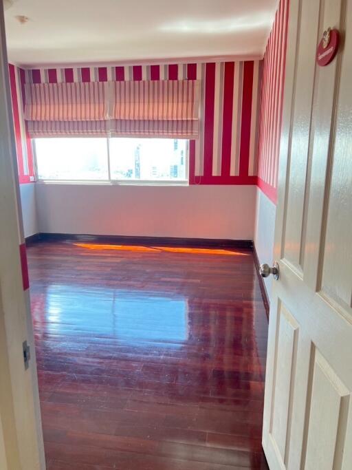 Empty bedroom with wooden floor and striped red and white wallpaper