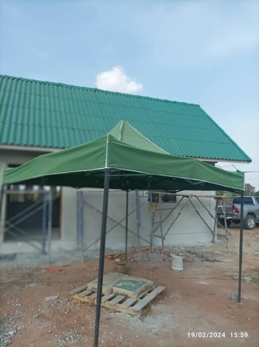 Exterior view of a building under construction with a green roof and canopy