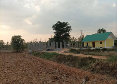 Wide view of a plowed field, adjacent to a partially built structure and a small house.